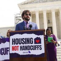 Jesse Rabinowitz standing at podium with a sign that reads "Housing Not Handcuffs"